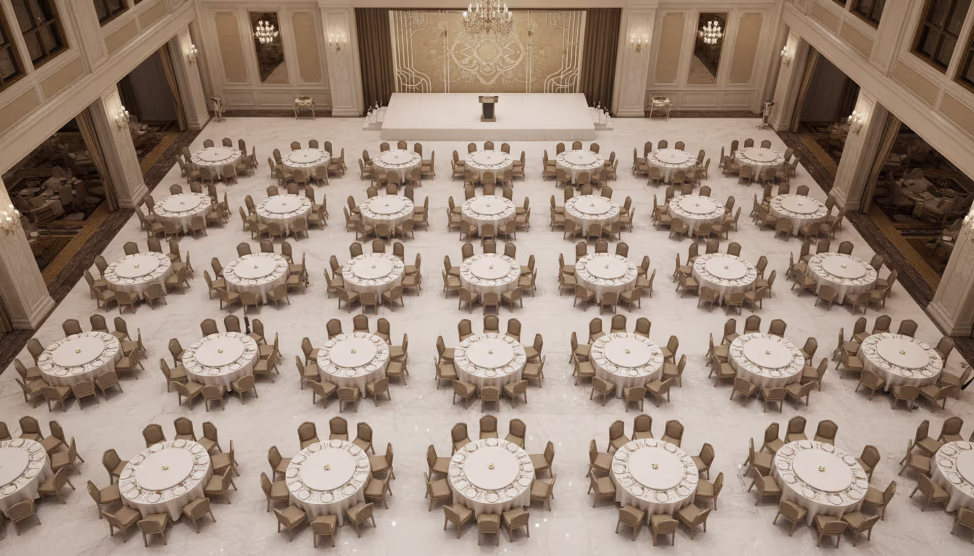 Aerial view of an elegant banquet hall with round tables covered in white tablecloths arranged symmetrically with a stage at the far end