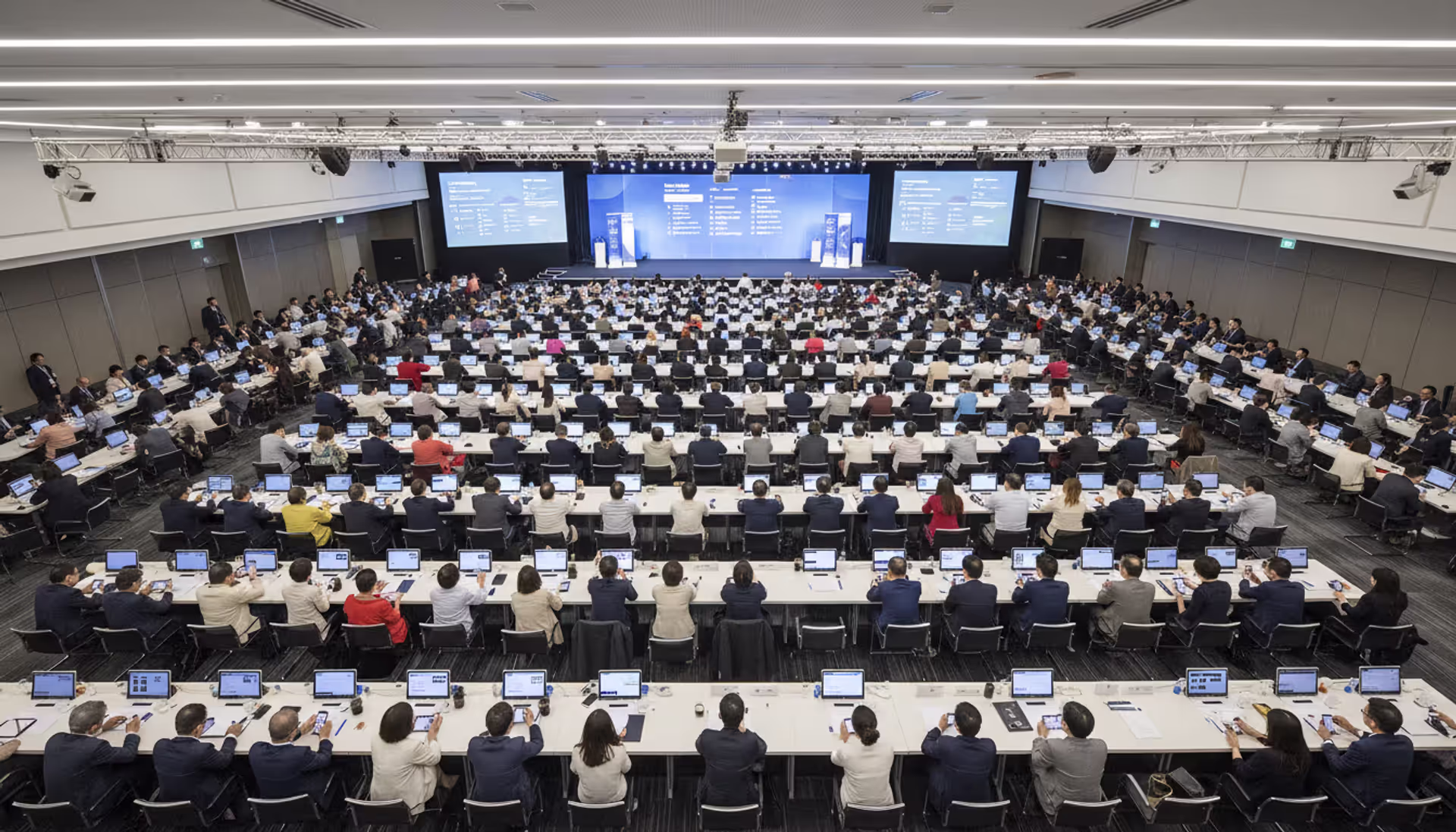 Aerial view of a large conference hall with attendees using smartphones displaying event schedule app interfaces